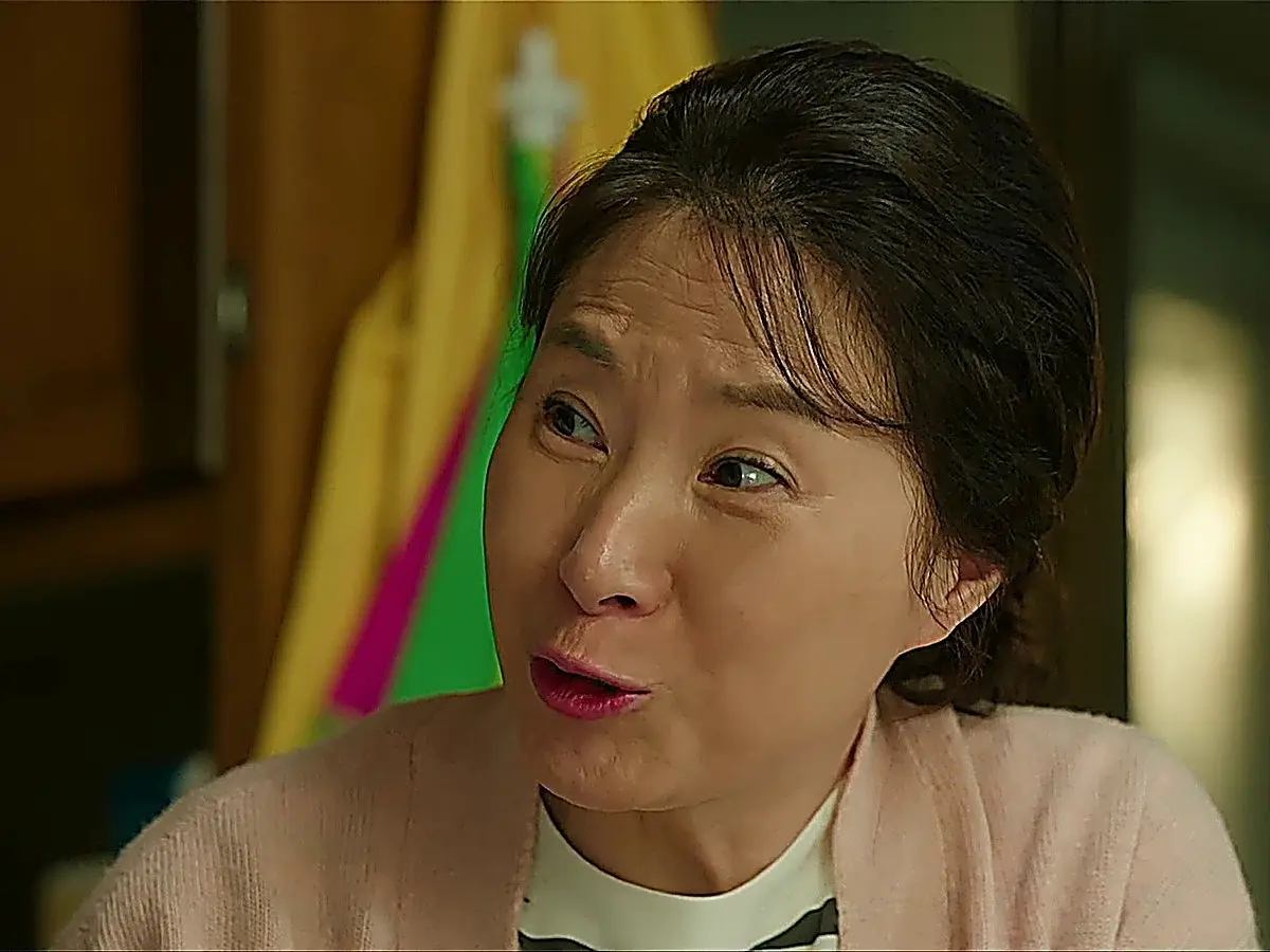 Woman in a light pink cardigan speaking animatedly indoors
