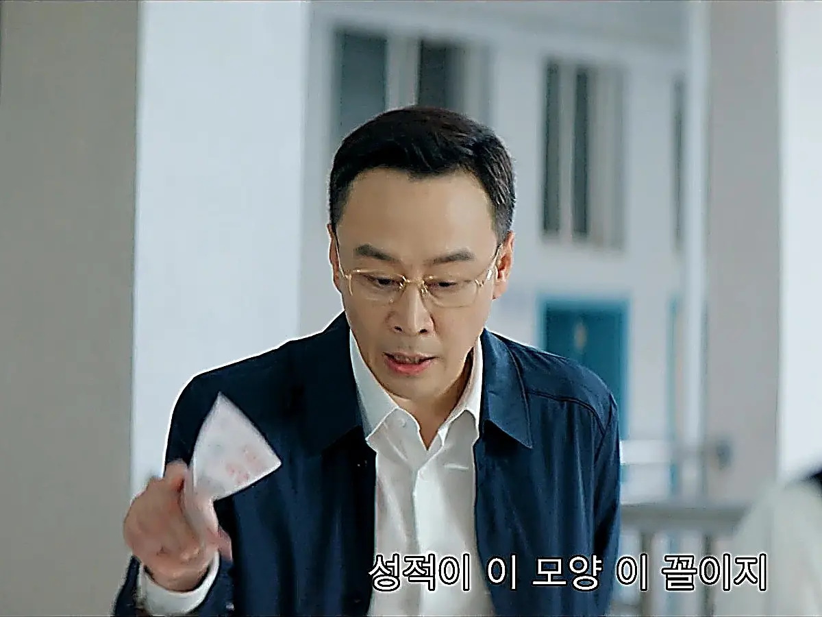 A man wearing eyeglasses and a navy jacket holding folded papers in a hallway