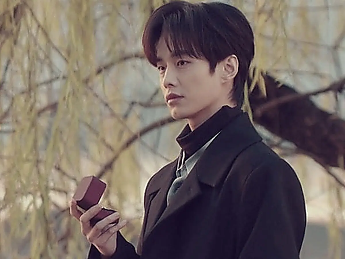 Jin Zhao holding a ring box in a black tailored overcoat