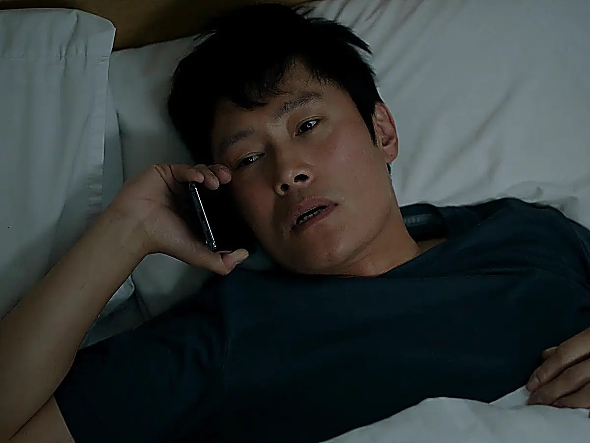 A man lying back on white bedding while speaking into a mobile phone