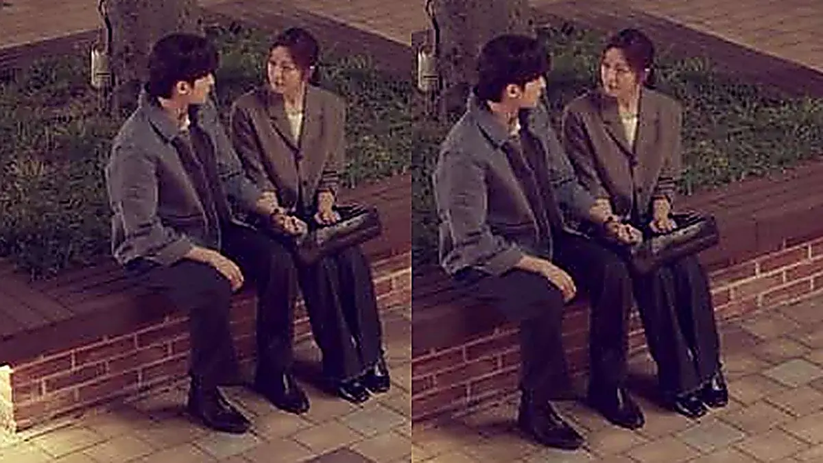 A man in a denim jacket and a woman in a grey tailored blazer sitting together on an outdoor bench holding hands
