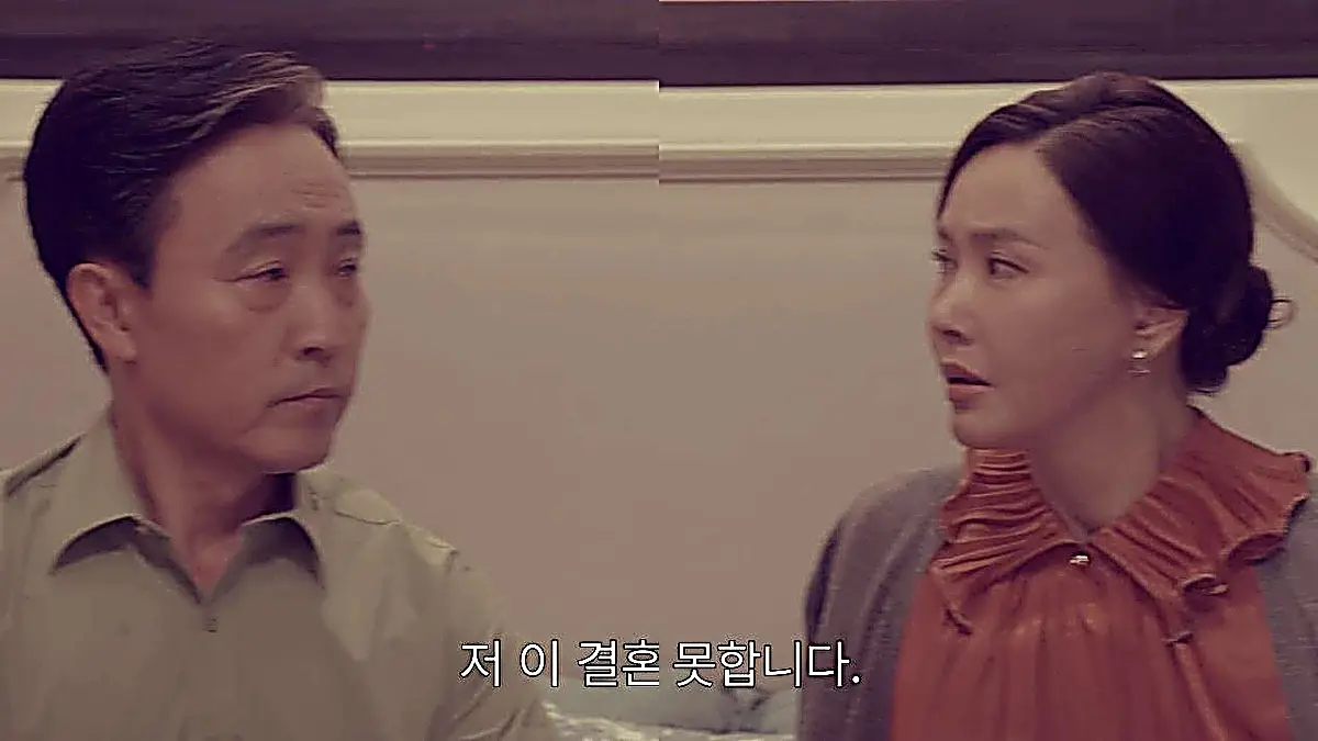 A middle-aged man in a green shirt and a woman in an orange pleated blouse looking surprised
