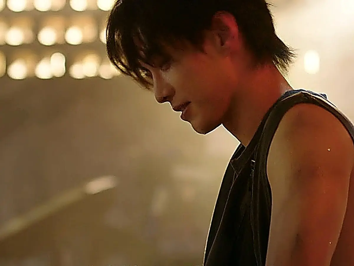 Jin Zhao looking downward with a subtle grin in a sleeveless top under warm indoor lights