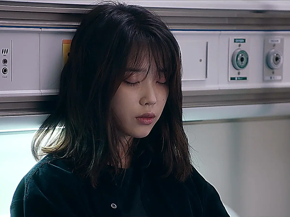 A young woman with shoulder-length hair leaning against a medical room wall panel with closed eyes