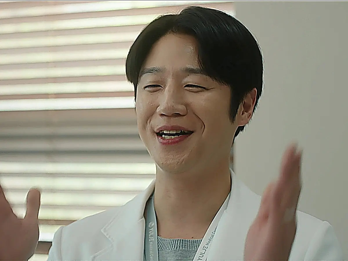Koo Do-won applauding in a white doctor coat layered over a light grey knit top