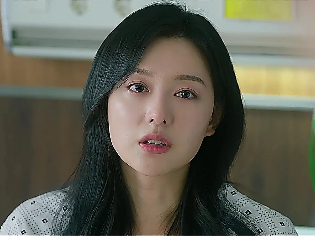 Close-up of a woman with long black hair wearing a patterned collared top looking forward with teary eyes