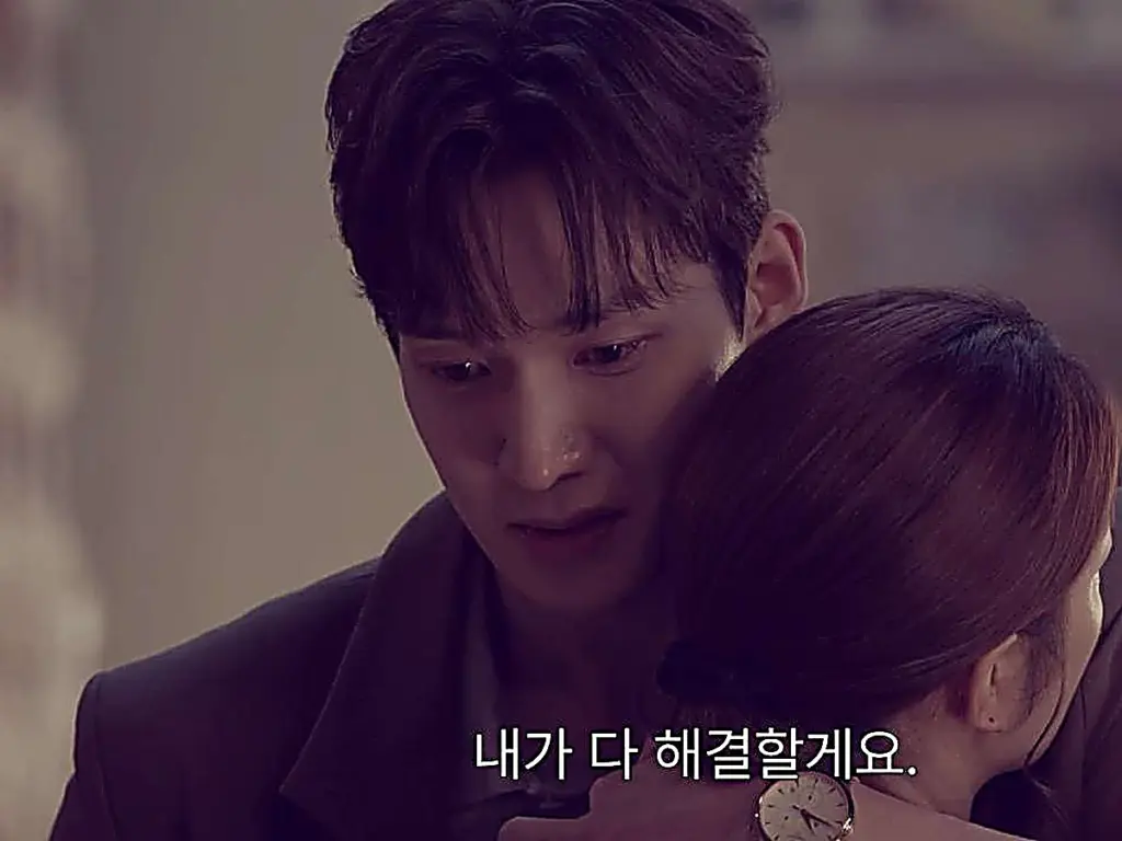 A man with dark hair in a dark tailored jacket embracing a woman while looking down with tearful eyes.