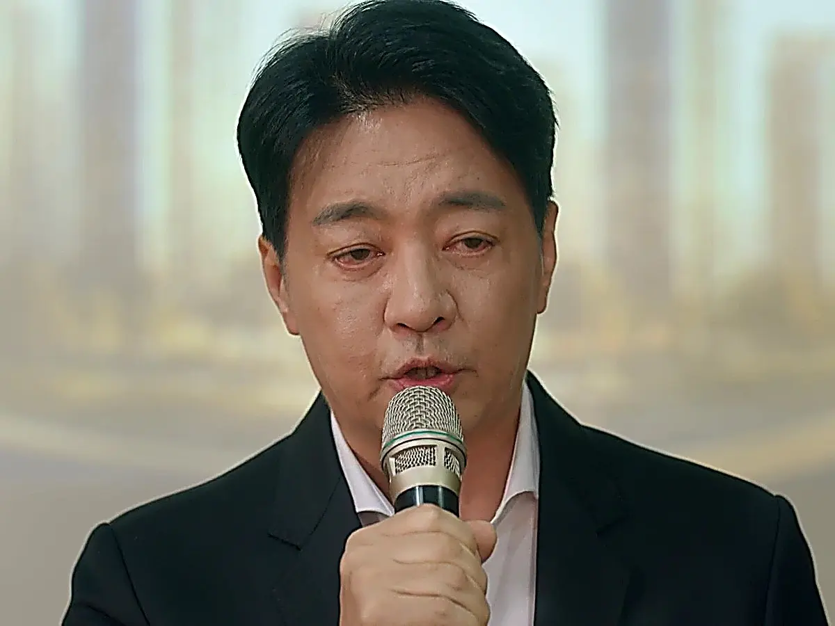 Ko Dae-chi speaking at the podium in a tailored black suit jacket