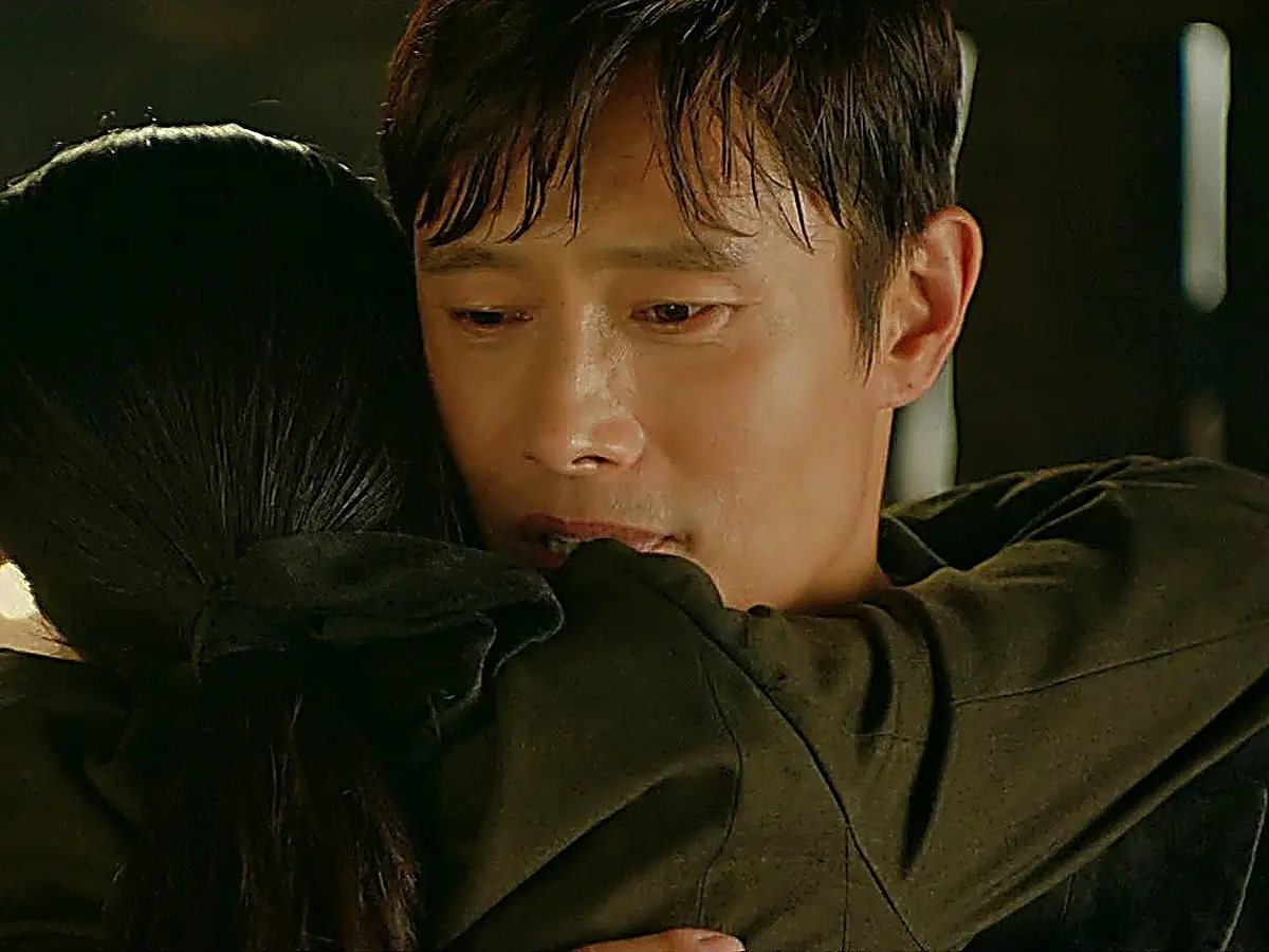 A man with dark hair embracing a woman with tied-back hair from behind