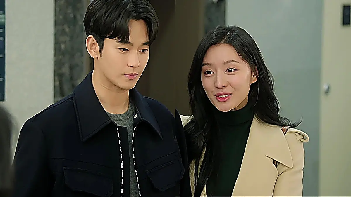 Baek Hyun-woo in a dark navy zip jacket and grey knit next to Hong Hae-in in a beige coat and dark turtleneck