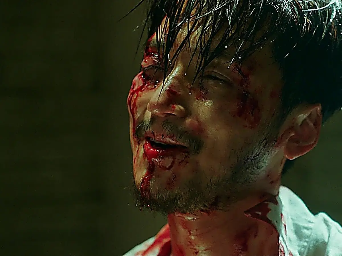 A bruised and bloodied man with damp hair smiling faintly despite visible injuries
