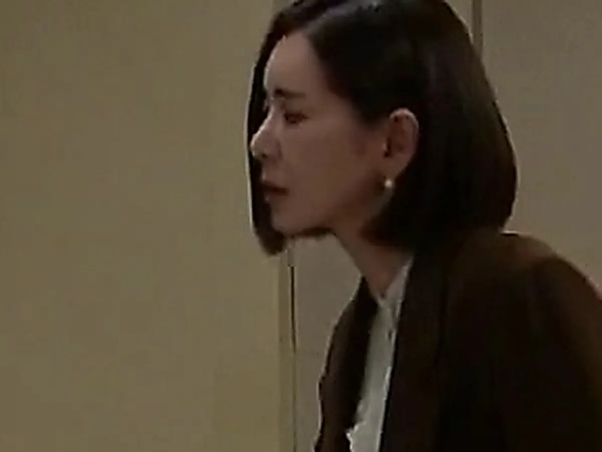 Side profile of a woman with short hair wearing a brown blazer standing beside a closed doorway.