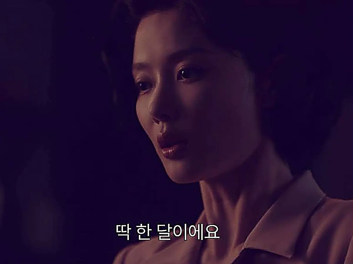 A woman with curled hair wearing a tailored collared blouse looking sideways in low lighting