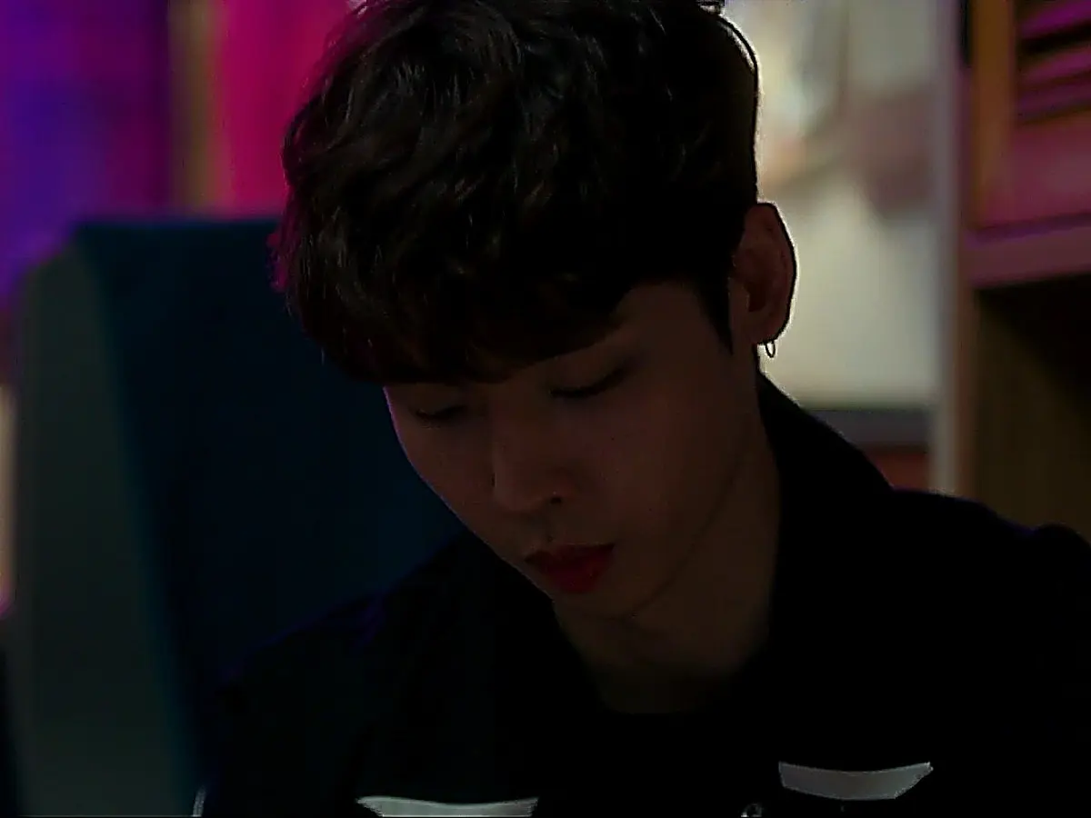 A young man looking downward in dim lighting