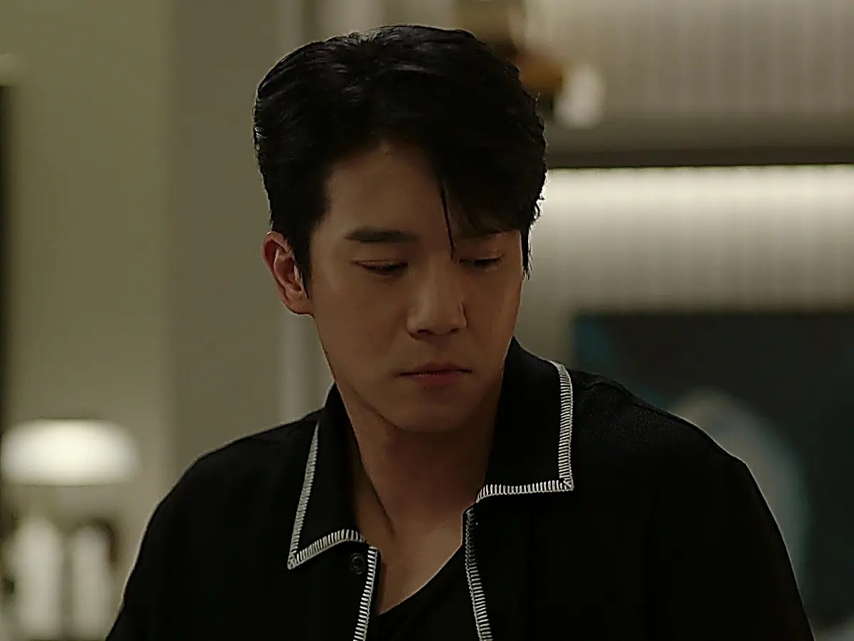 Mu-jin wearing a black collared knit shirt with white contrast stitching along the collar