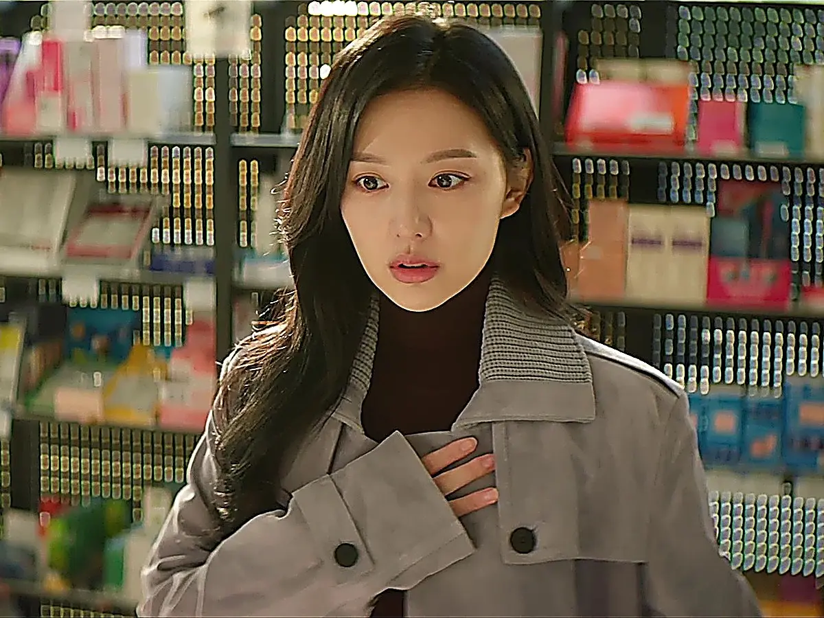 Hong Hae-in wearing a grey belted trench coat over a dark knit turtleneck in a store