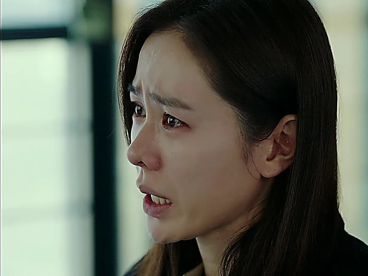 A woman with dark hair in profile speaking with tears in her eyes.