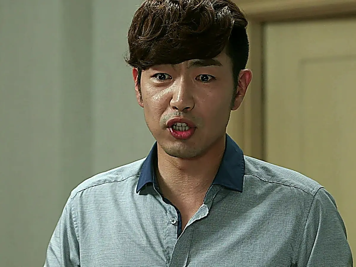 A man in a grey collared shirt with blue collar trim speaking with an intense expression