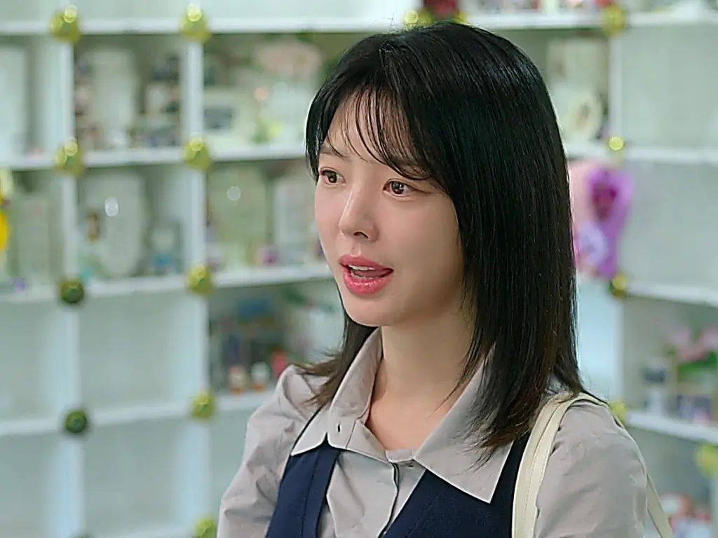 Jo Eun-ae wearing a grey pointed-collar button-down shirt layered under a navy vest with a cream shoulder strap