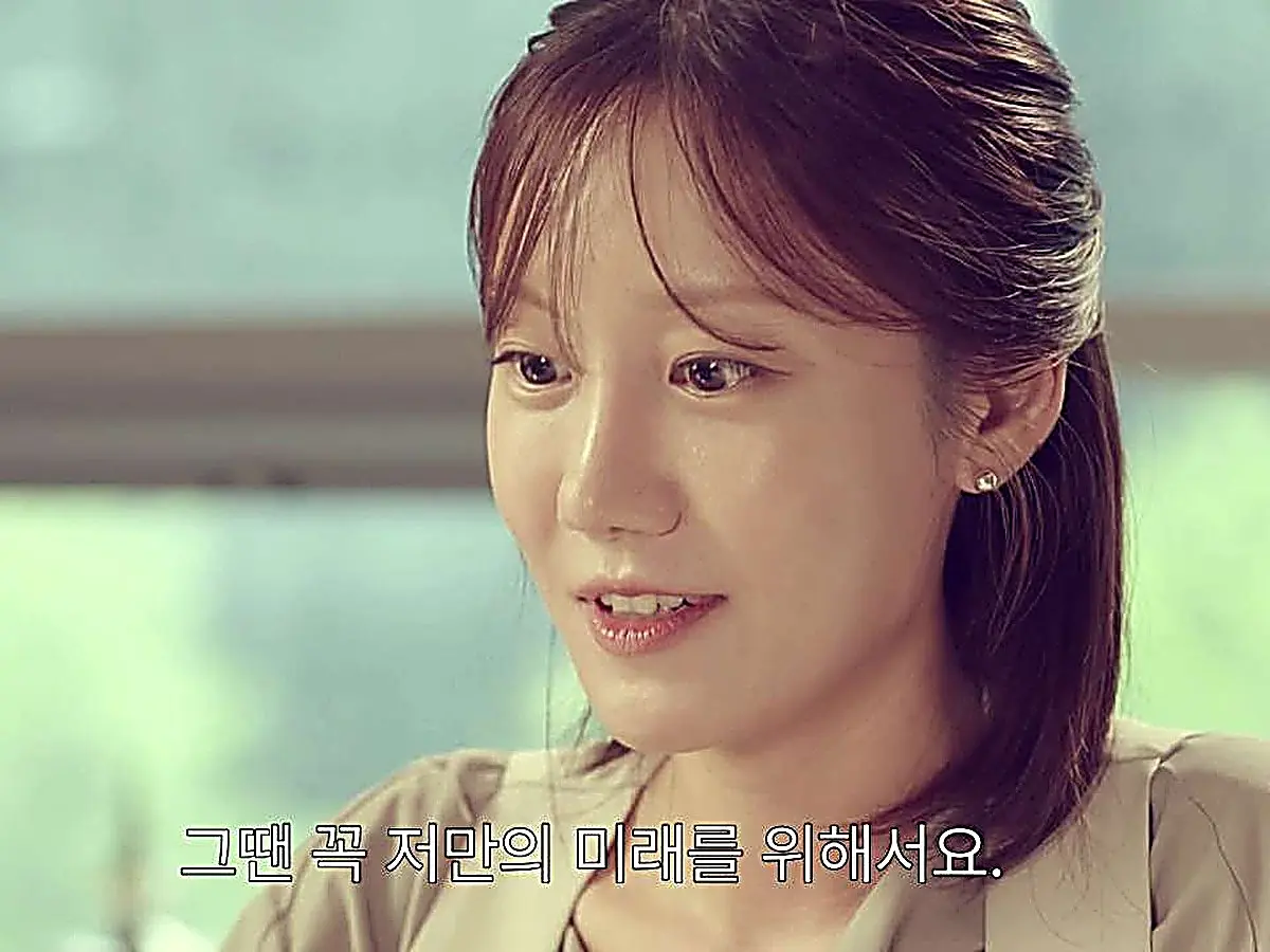 A woman with bangs and ponytail wearing a light blouse smiling softly with glistening eyes