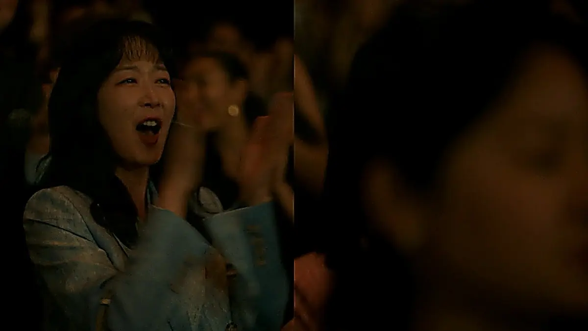 Woman in a light blue textured jacket applauding in a concert hall audience