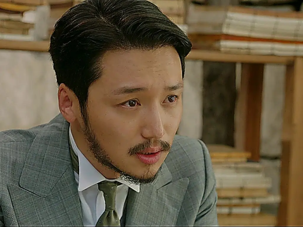 Kim Hui-seong wearing a grey tailored suit with wide lapels and a green silk tie