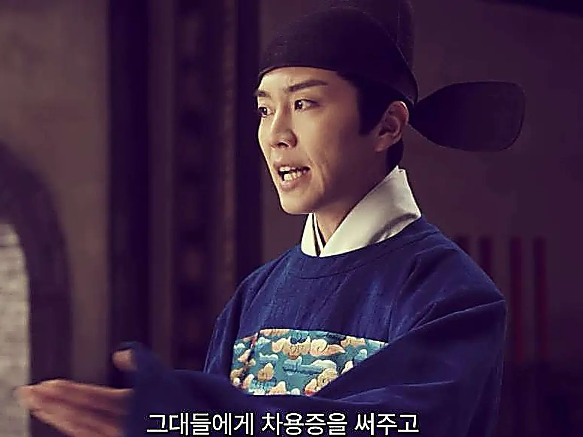 A man in a dark blue official robe and winged cap gesturing while speaking