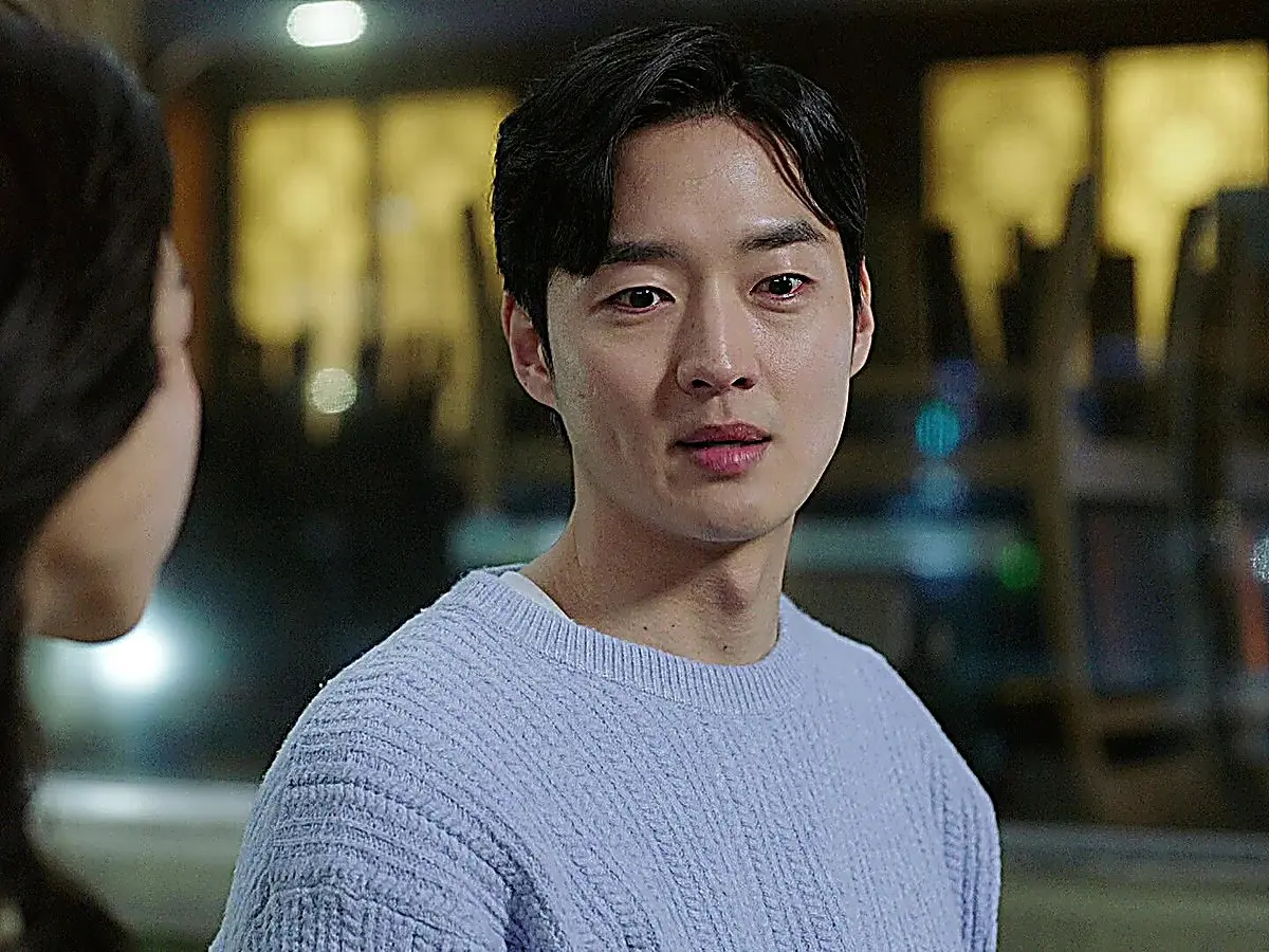A young man wearing a light blue knitted sweater speaking softly while gazing ahead at night