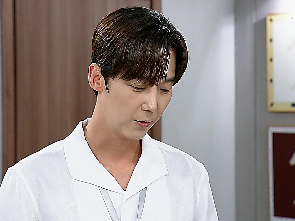 A young man with parted brown hair wearing a white collared shirt looking downward with a pensive expression