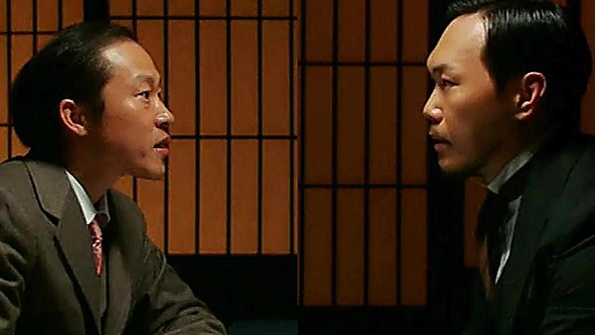 Two men in western suits seated in profile facing each other indoors