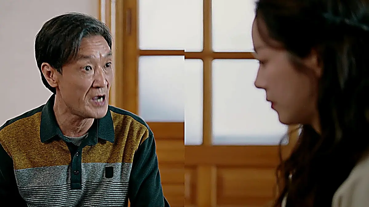 Park Jeong-jun's father wearing a collared knit polo shirt with an olive green collar, heather grey stripe, and patterned lower panel speaking to Lee Young-ok