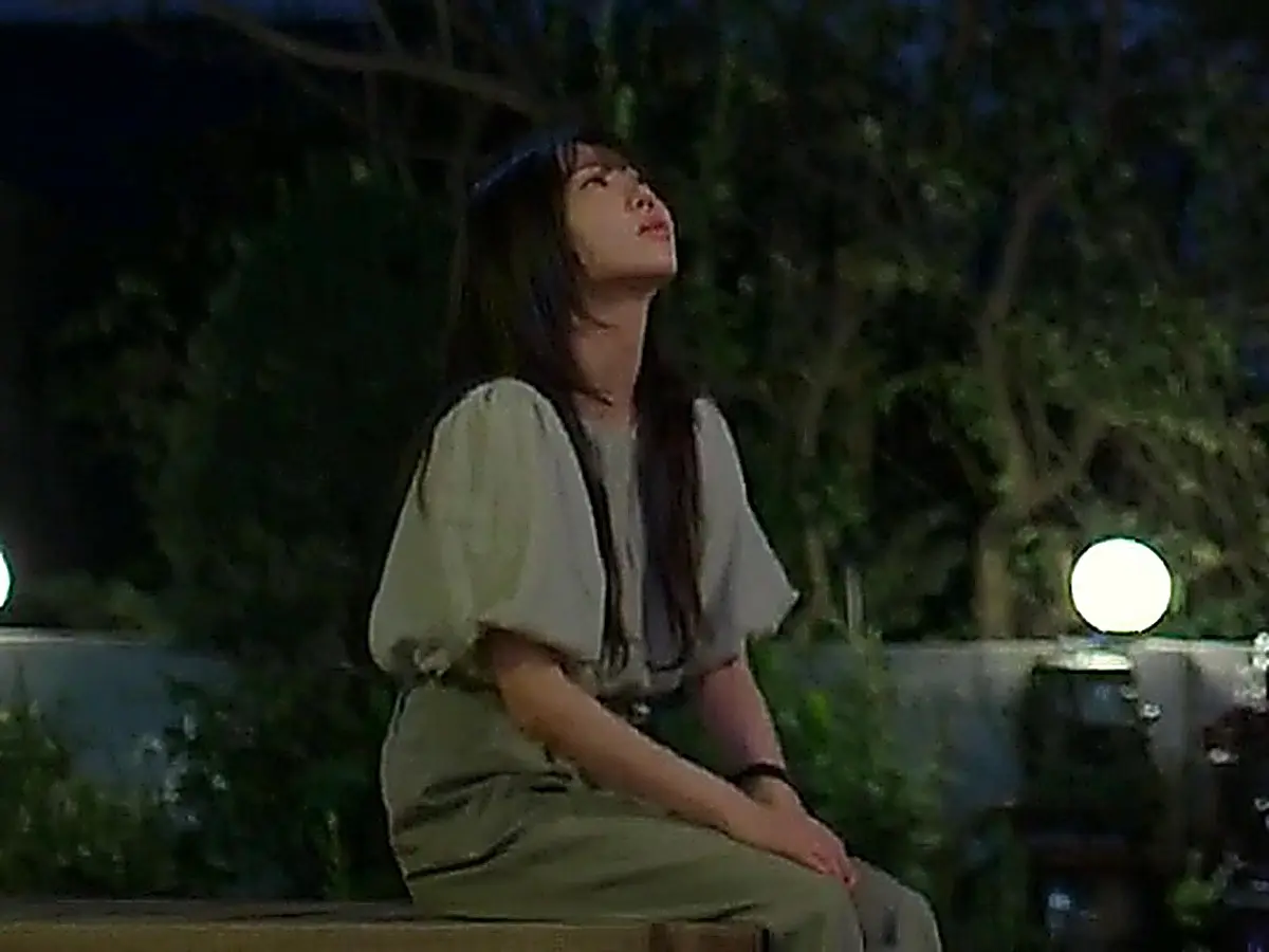 Go Eun-seol sitting on an outdoor bench at night wearing a short-sleeve gathered blouse and belted olive trousers