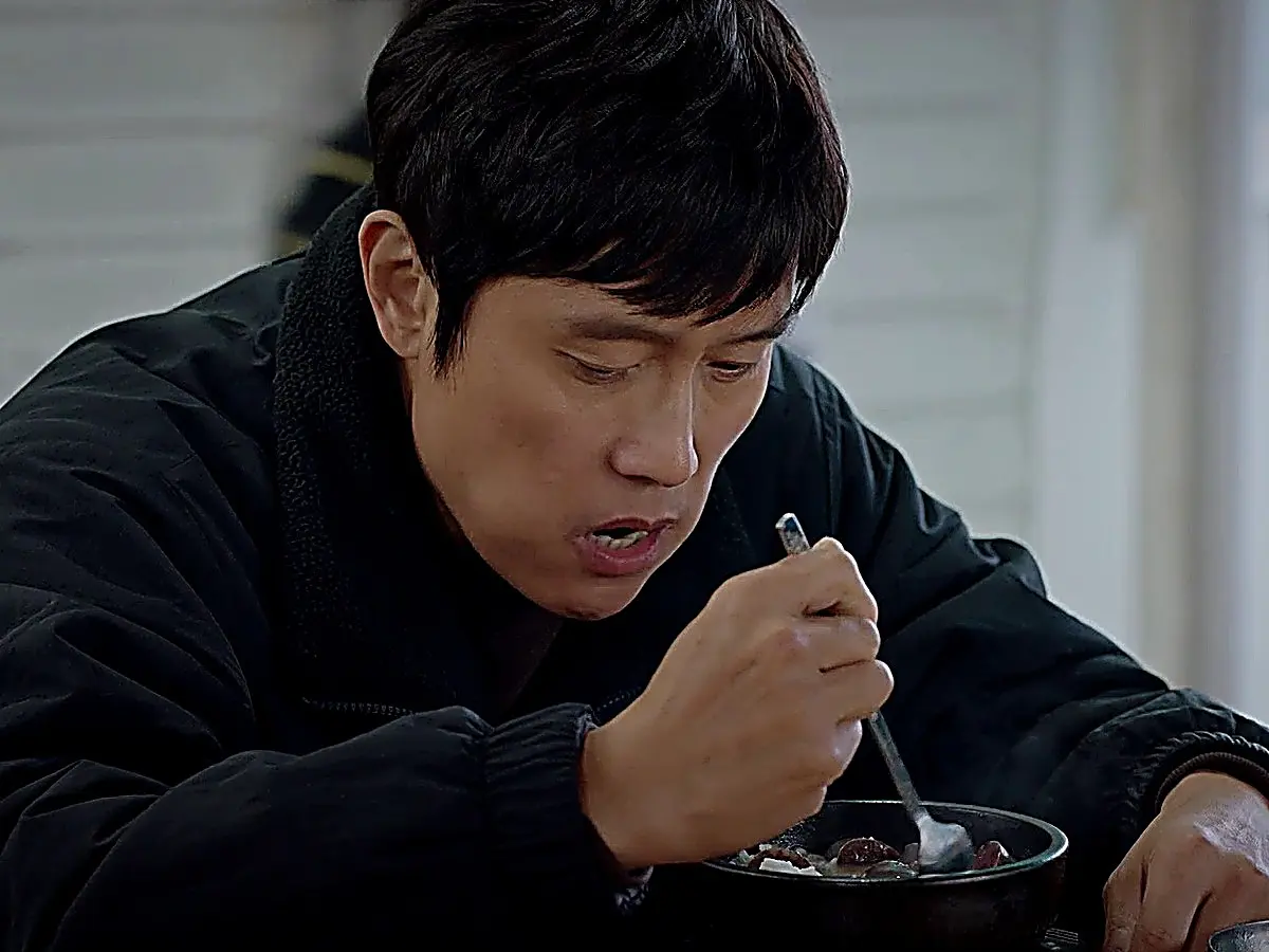A man eating from an earthenware bowl with a spoon while wearing a dark jacket