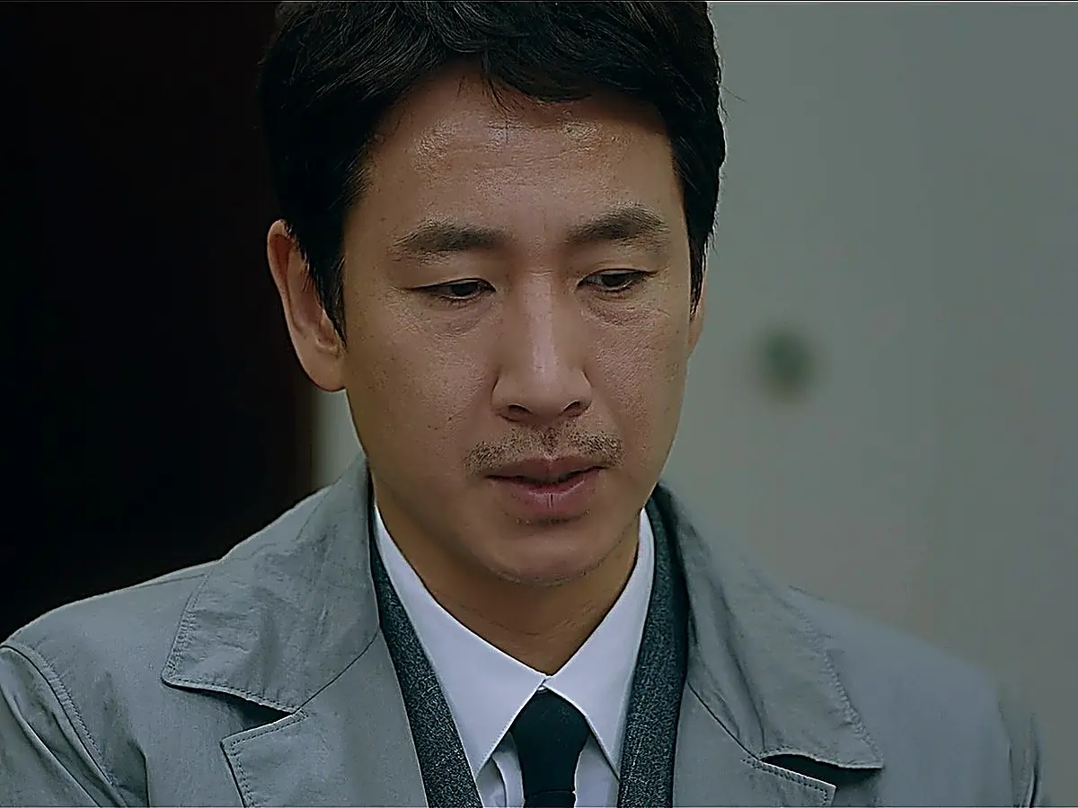 Park Dong-hoon wearing a tailored grey coat over a white collared shirt and dark tie