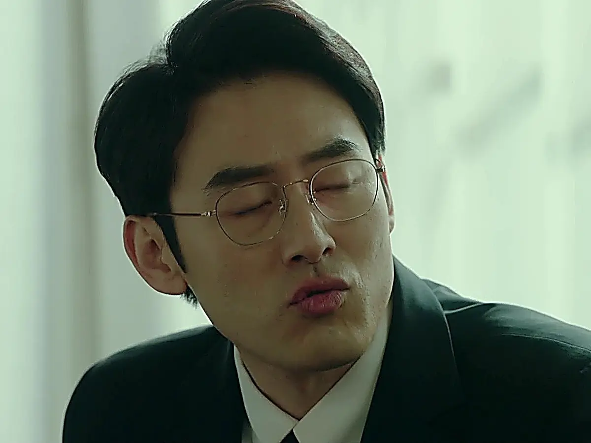 Yoon Se-hyung wearing thin wireframe glasses and a tailored black suit jacket over a white collared dress shirt
