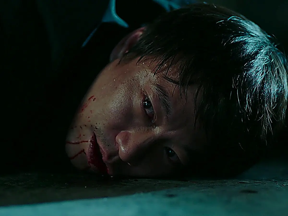 A man lying on the pavement with visible injuries and blood traces around his mouth.
