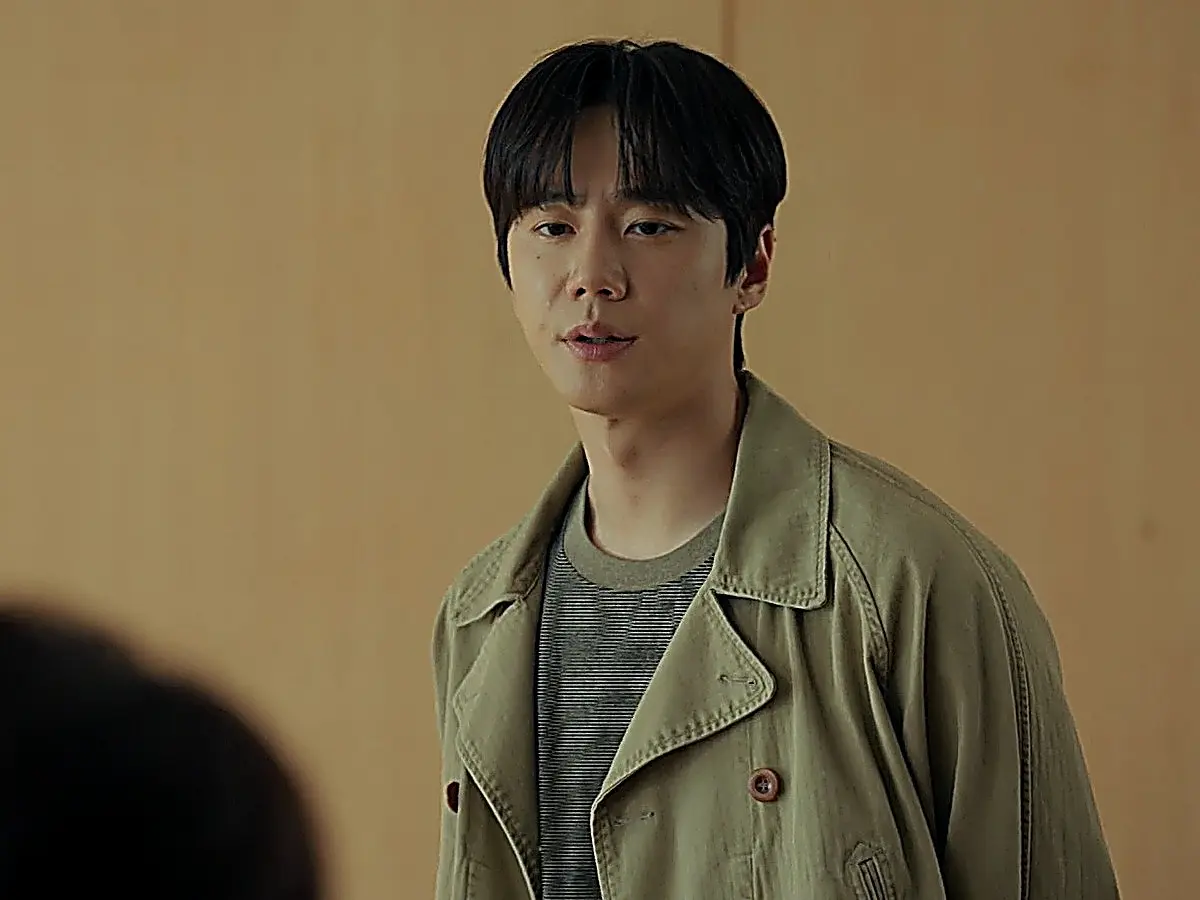 Choi Jeong-yo in a double-breasted khaki trench coat with tortoiseshell buttons and a fine striped tee
