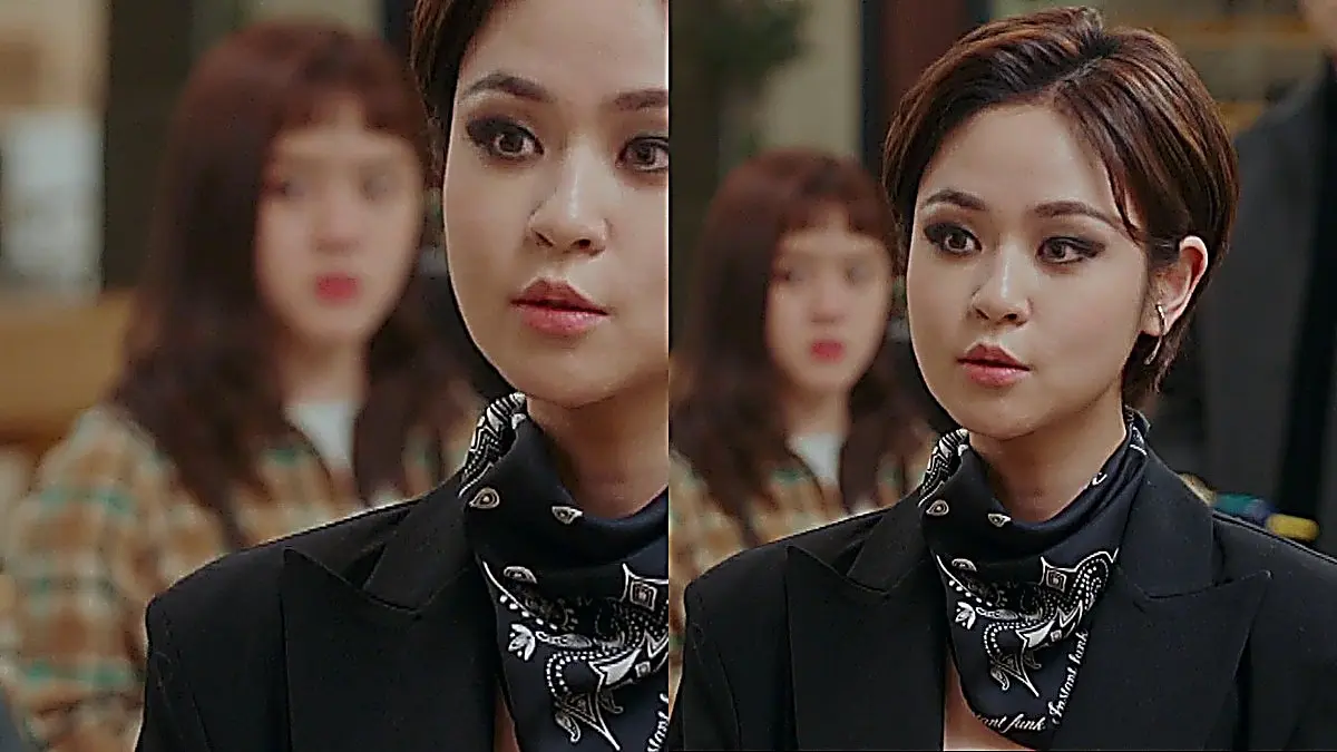 Designer Jen in a black fitted blazer and bandana confronting a client in the salon
