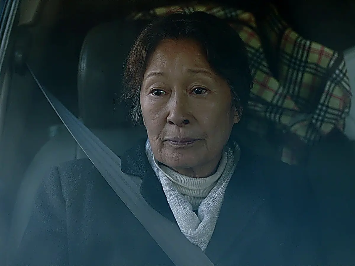 Kang Ok-dong stares pensively through the truck passenger window