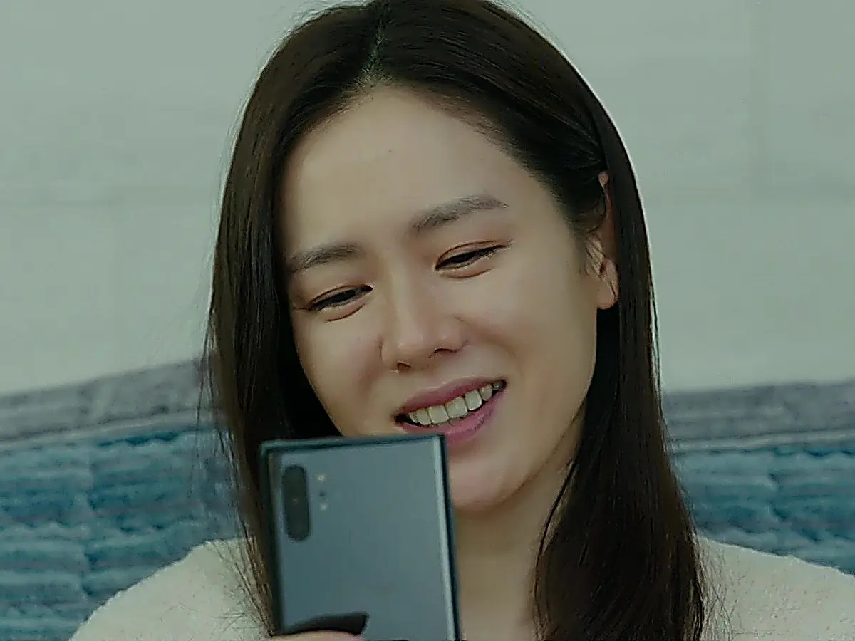 A woman with long dark hair smiling while looking down at a mobile device