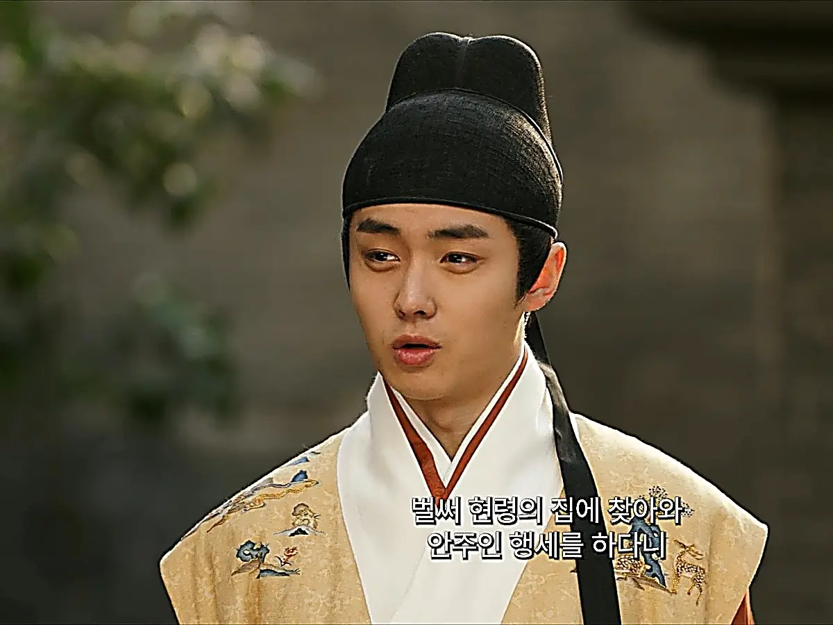 Qi Menglin wearing a gold embroidered robe with an inner white crossover collar and structured black headwear