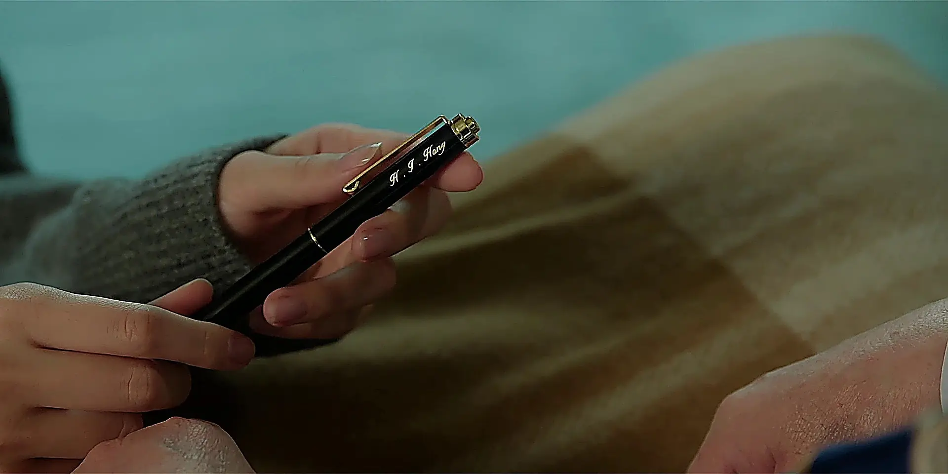 Hands holding a black fountain pen with gold clip engraved with initials H. I. Hong