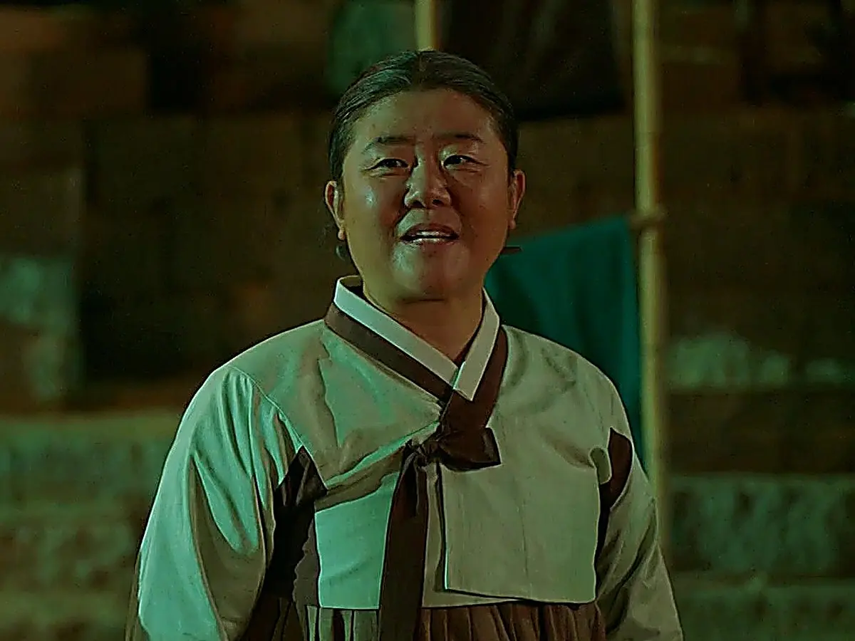 A woman wearing a light-colored traditional hanbok smiling under night lighting