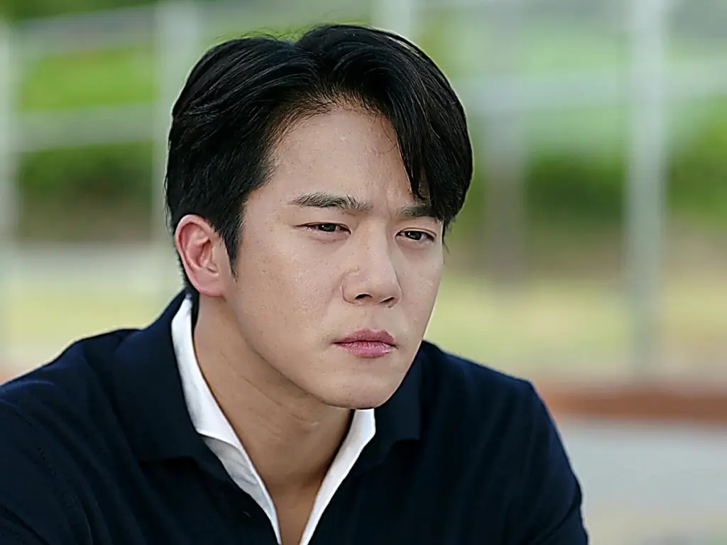 Mu-jin wearing a navy collared knit polo layered over an open white collar shirt