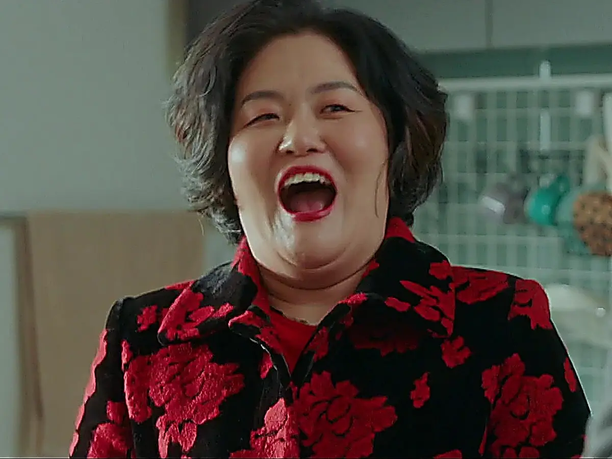 A woman laughing with mouth open wearing a black coat with red floral patterns