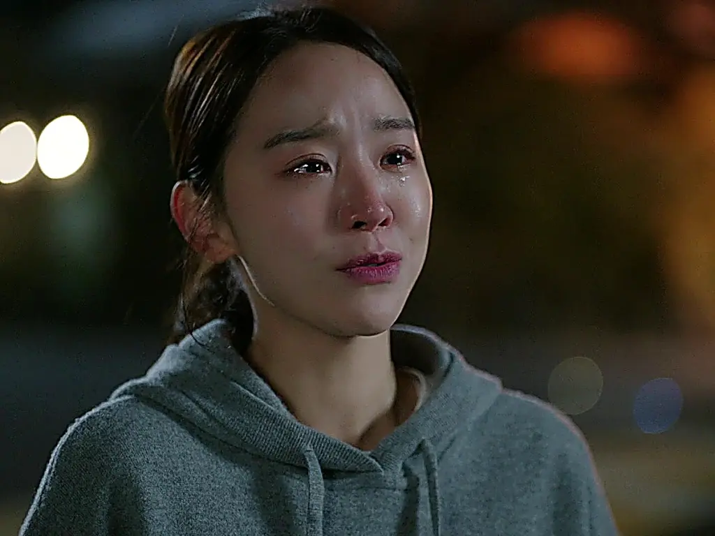 A woman wearing a grey hooded sweatshirt with tears on her face in an outdoor night setting